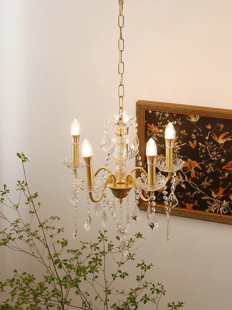Gold chandelier with crystal accents on a neutral wall with a decorative painting and plant.
