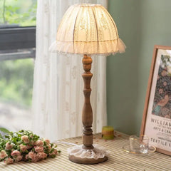 Side view of a wooden table lamp with a lace shade, showcasing its base and stem.