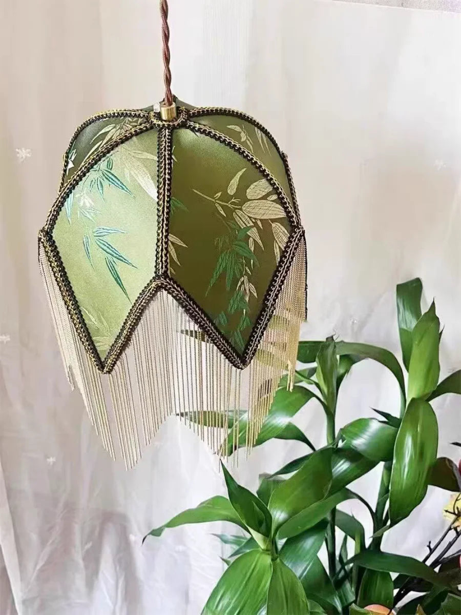 Decorative hanging lamp with green glass and gold accents next to a plant 
