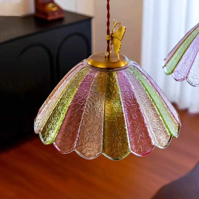 Decorative lamp with colorful glass shade and butterfly finial on a wooden surface.