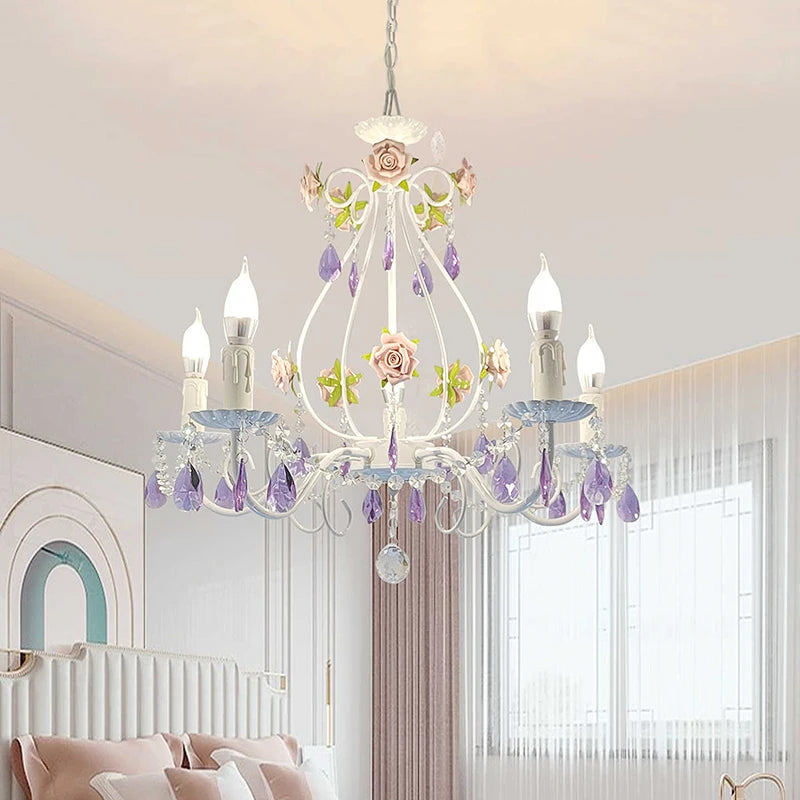 White wrought iron chandelier with pink floral accents and purple crystal teardrops hanging in a bedroom.