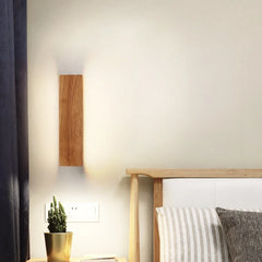 Wooden wall sconce mounted on a white wall above a nightstand with a potted cactus and books, next to a bed with striped pillows.