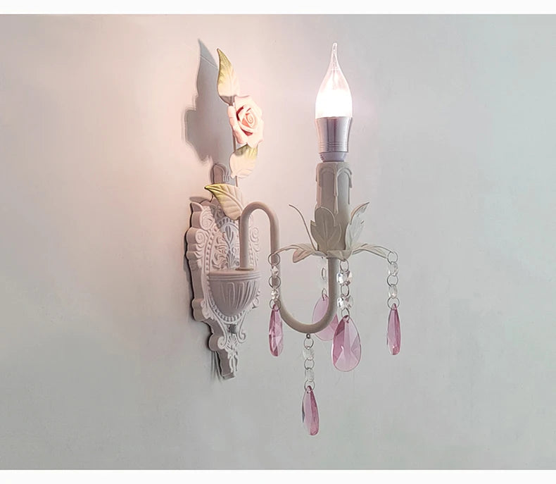 Close-up of a white wall sconce with pink crystal droplets, highlighting the intricate floral details and the LED bulb.