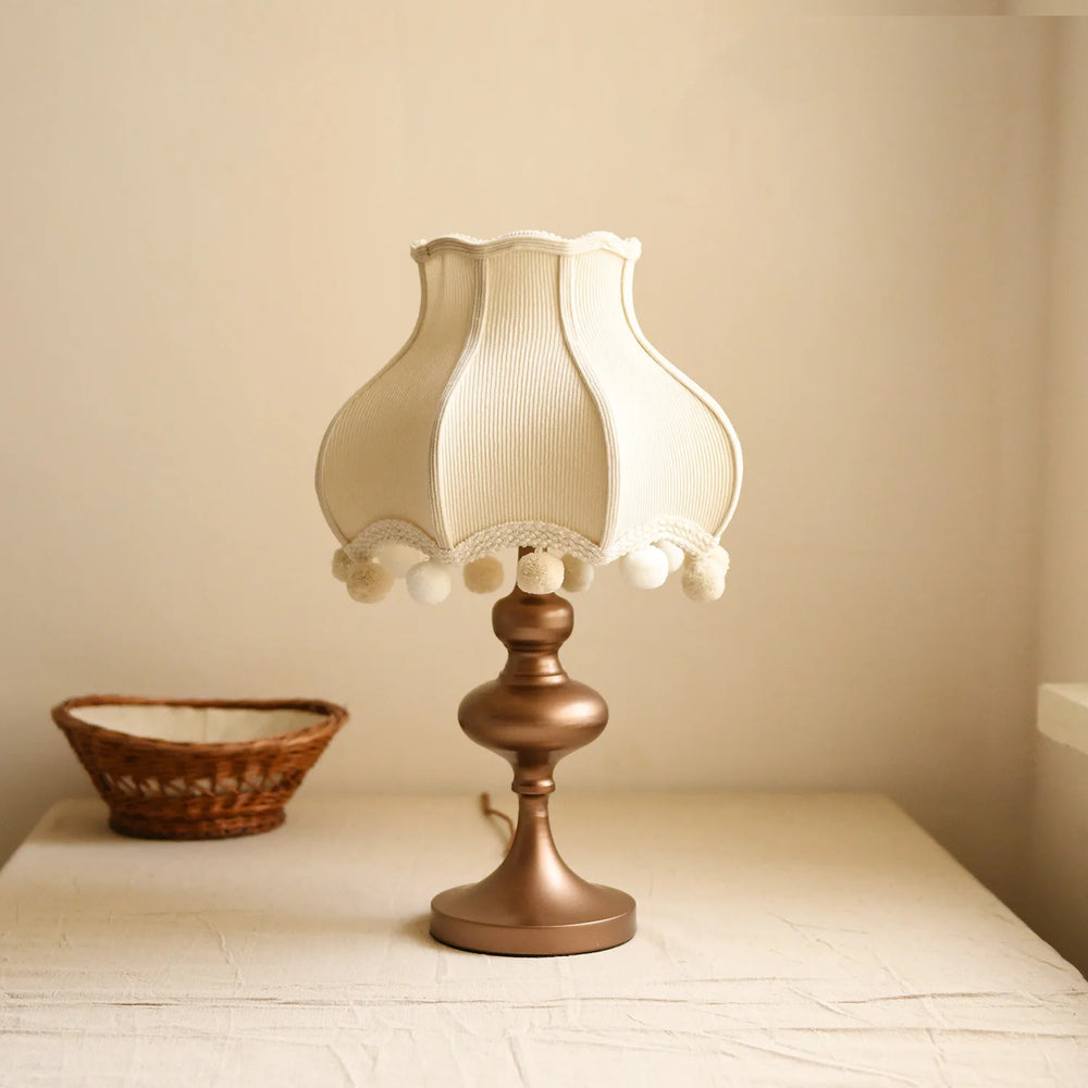 Table lamp with lace detailing on a wooden surface against a beige wall