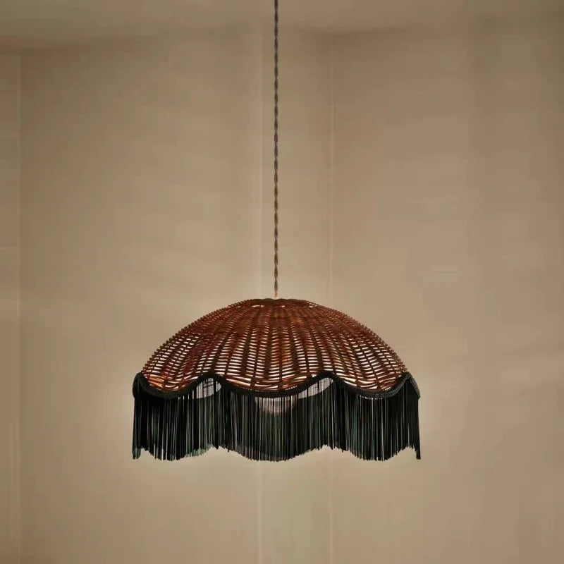 Woven rattan dome pendant light with a dark fringe hanging against a plain background