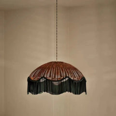 Woven rattan dome pendant light with a dark fringe hanging against a plain background
