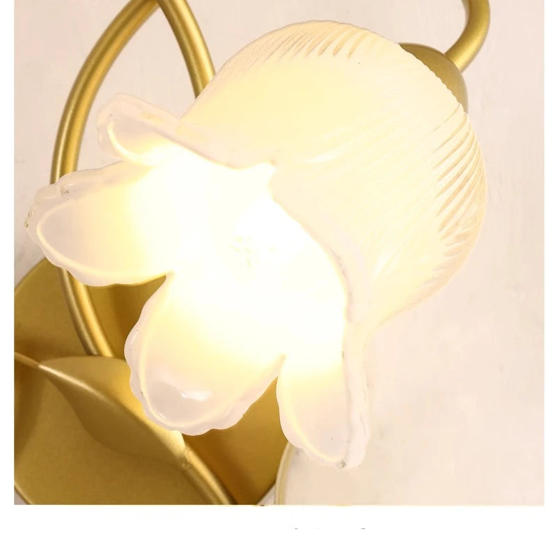 Decorative wall light fixture with gold frame and white glass shades on a plain background