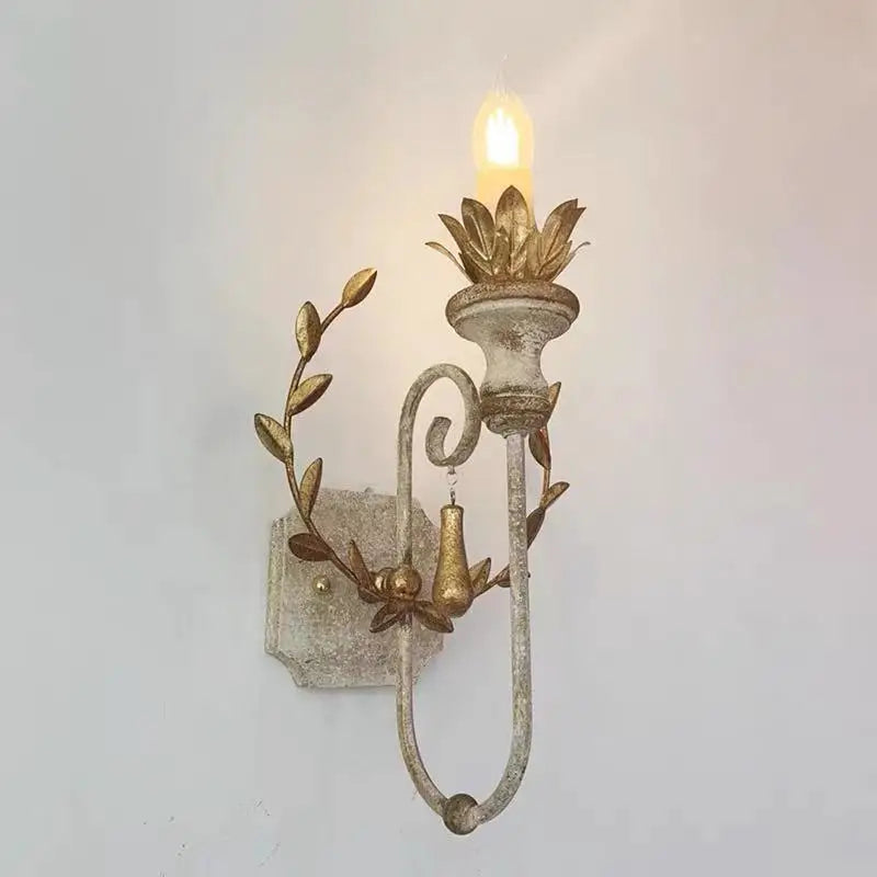Side view of a distressed gold metal wall sconce featuring a leaf wreath and a candle-style LED bulb, mounted on a white wall.