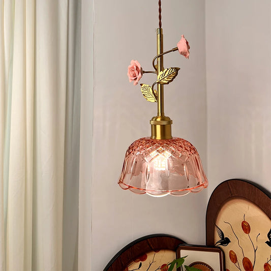 Close-up of a pendant light's brass stem with pink ceramic roses and green leaves, above a pink glass shade.