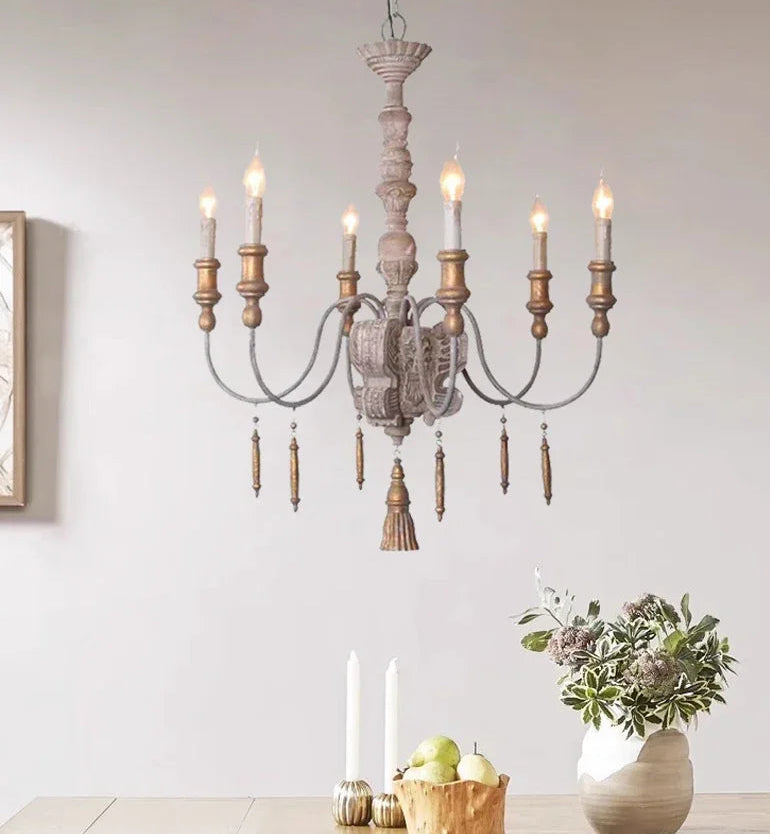 Wooden chandelier with candles in a room setting with a table and decor items.