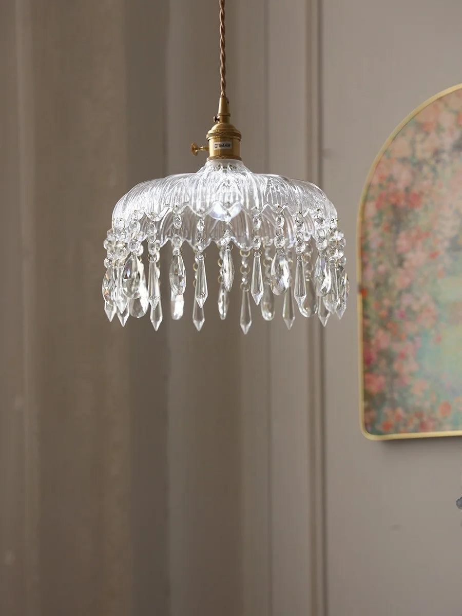 Crystal pendant light hanging against a neutral wall with a decorative mirror.