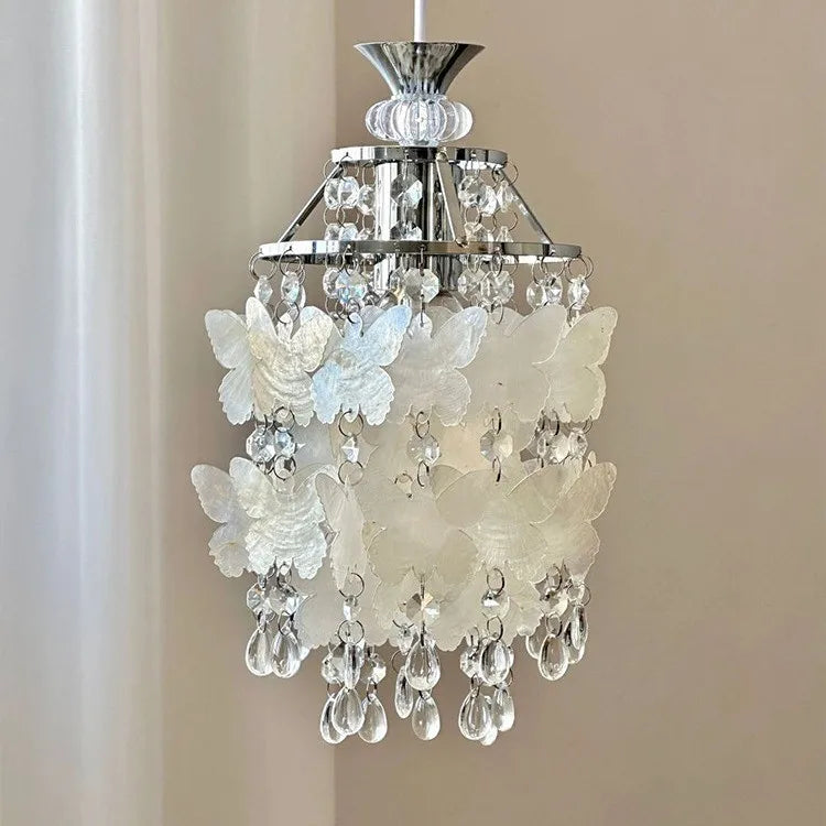 Side view of a chrome pendant light adorned with white butterfly shell decorations and crystal droplets.