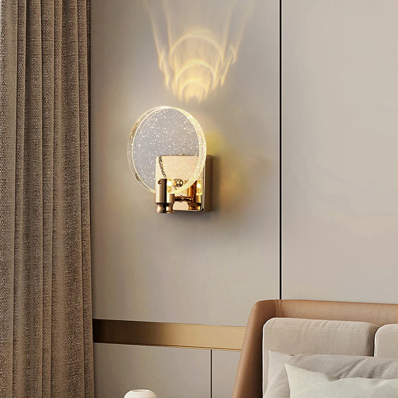 A gold and clear bubble crystal wall sconce mounted on a light gray wall next to a grey curtain in a bedroom.