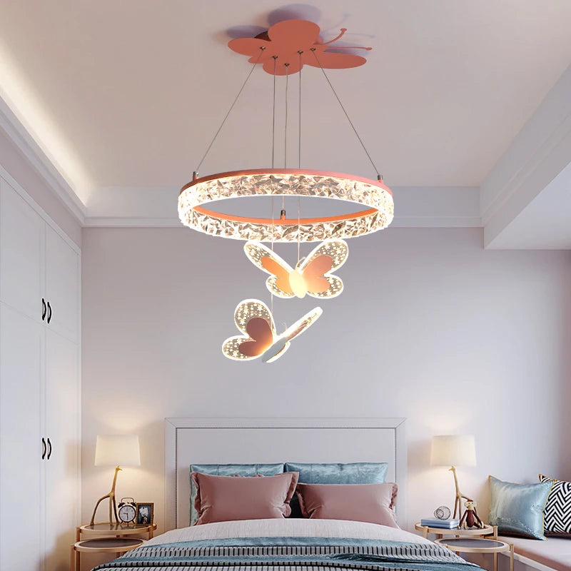 A pink crystal ring pendant light with butterfly accents hanging above a bed in a child's bedroom.