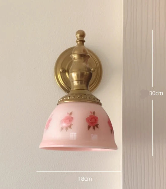 Wall lamp with pink glass shade and gold fixture on a neutral background