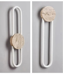 A wall sconce featuring a round stone piece and a U-shaped light element, shown against a grey wall.
