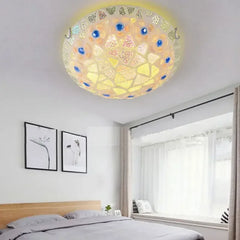 A mosaic glass seashell flush mount ceiling light installed on a bedroom ceiling above a bed