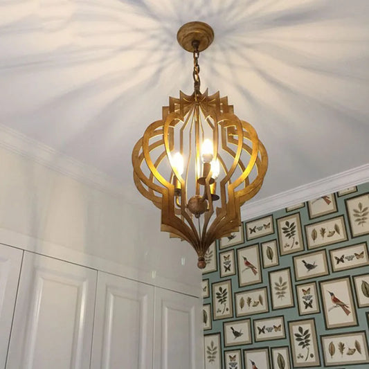 A gold geometric open frame pendant light installed on a ceiling, casting patterned light.