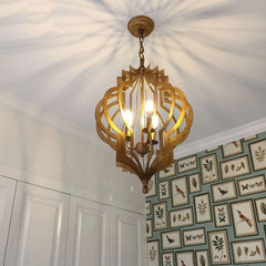 A gold geometric open frame pendant light installed on a ceiling, casting patterned light.