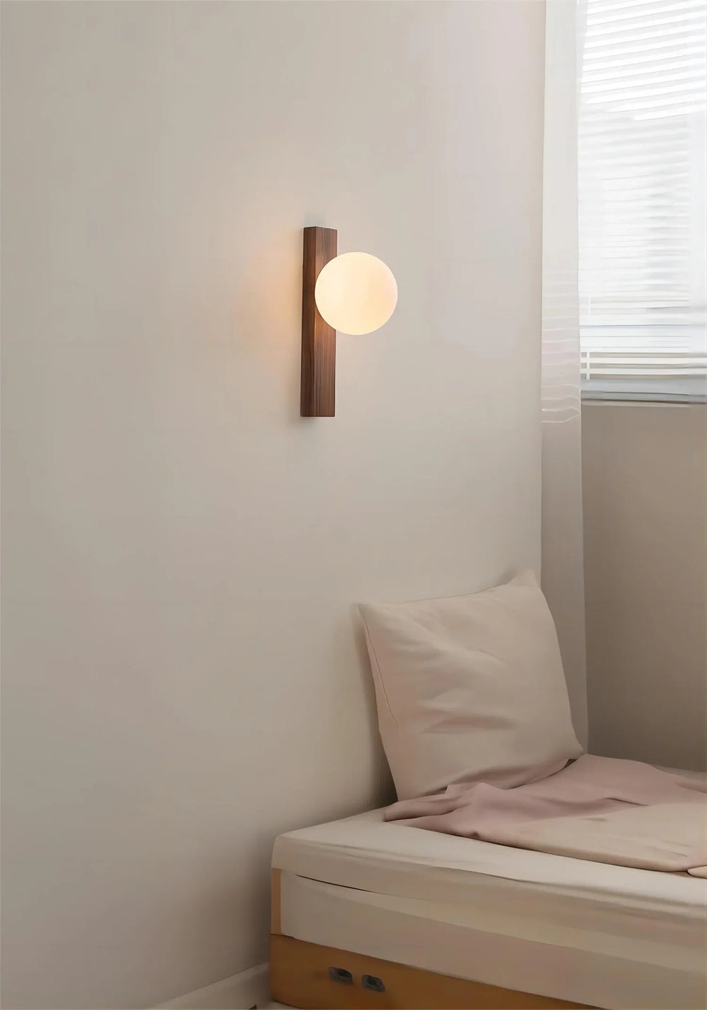 A cozy bedroom scene featuring a wood and frosted glass sphere wall sconce mounted above a bed with a white pillow and pink throw.