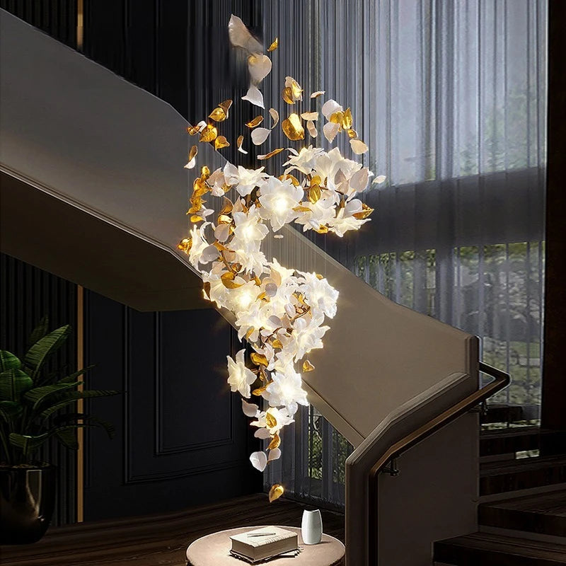 A cascading chandelier with gold floral and leaf accents and clear crystal droplets, illuminated and hanging near a modern staircase.