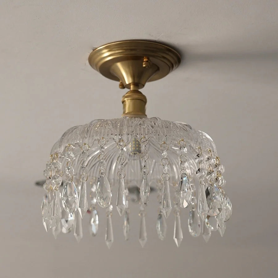Ceiling light fixture with clear glass shade and gold metal fixture on a neutral background