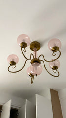 View from below of a gold and pink glass chandelier mounted on a white ceiling.