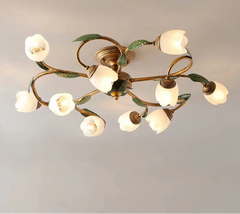 A close-up view of a gold multi-arm ceiling light with white tulip-shaped glass shades and green leaf accents, against a plain background.