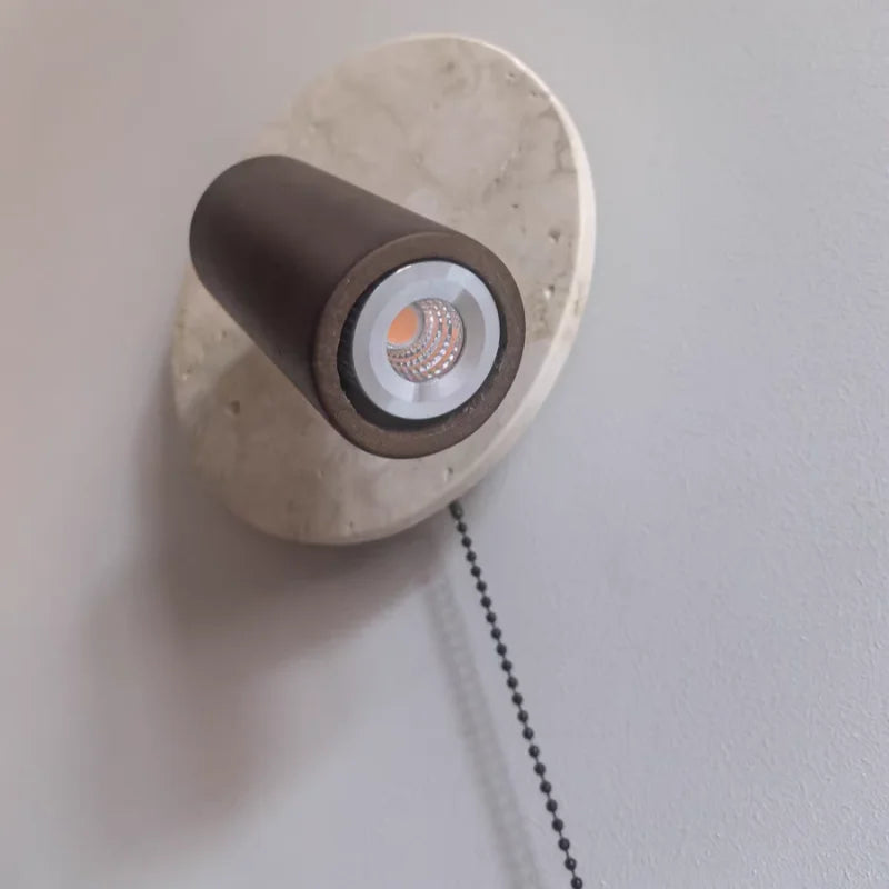 Wall-mounted light fixture with marble base and brown cylindrical shade on a plain wall.