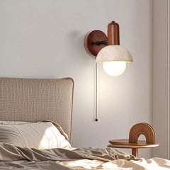 Close-up of a stone and wood wall sconce with a pull chain switch above a bed.