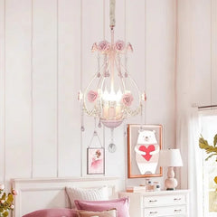 A pink crystal chandelier is featured in a bedroom setting with pink bedding and white furniture.