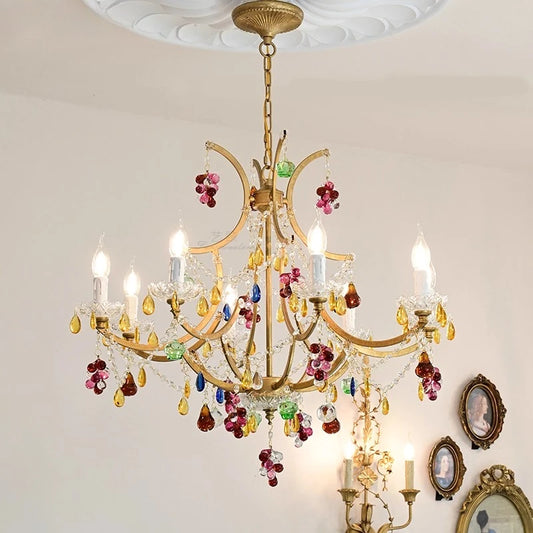 Close-up of a gold chandelier adorned with vibrant red, green, and purple crystals, with multiple light sources.