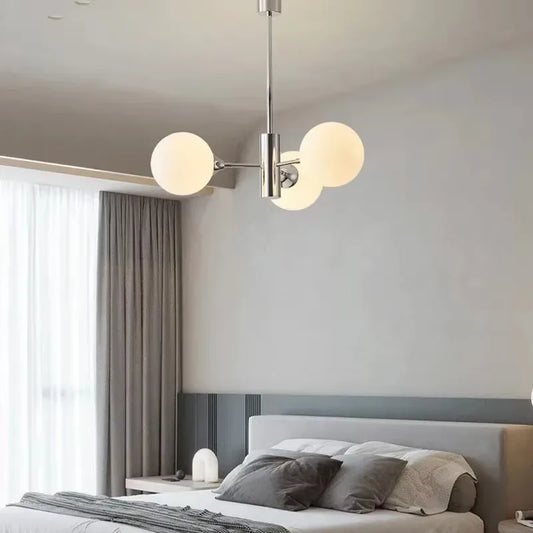 A polished chrome sputnik chandelier with frosted opal glass globes hanging above a bed in a modern bedroom with grey curtains.