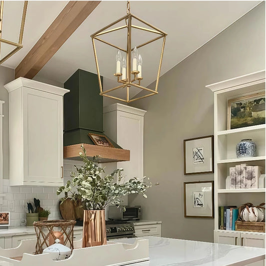 A gold geometric cage pendant light suspended from a chain in a modern kitchen setting with white cabinets and a green range hood.