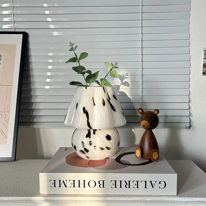 Decorative lamp with a plant and wooden bear on a book titled 'Gavire Boheme' against a window with blinds.