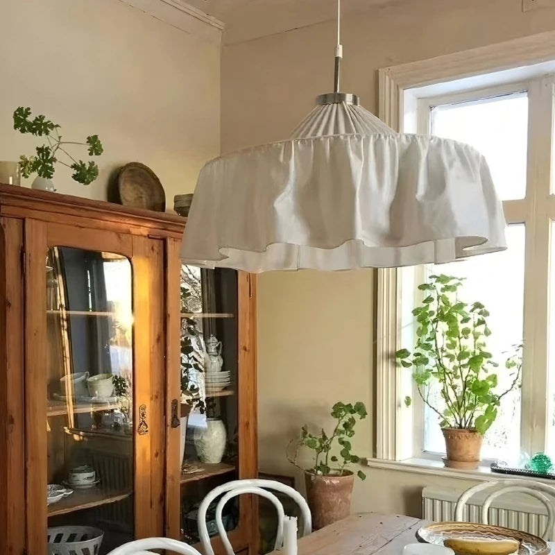 Close-up of a white pleated fabric pendant light illuminating a rustic dining room with a wooden cabinet.