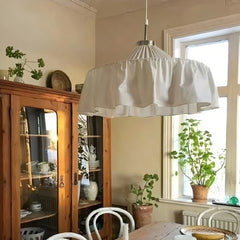 Close-up of a white pleated fabric pendant light illuminating a rustic dining room with a wooden cabinet.