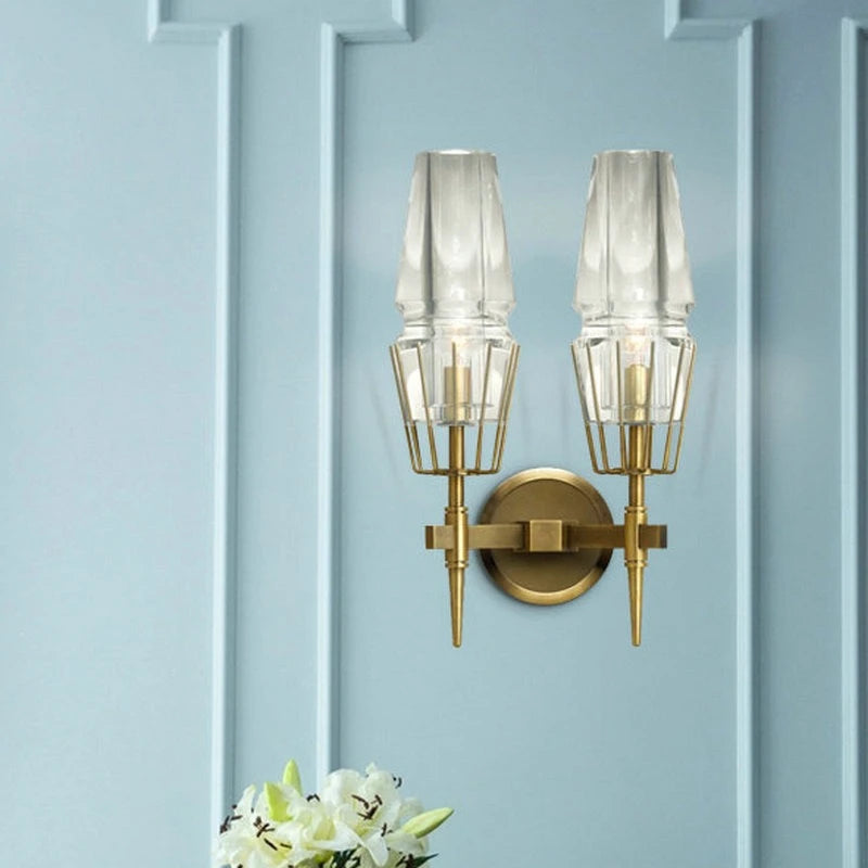 Two clear glass crystal wall sconces with brushed gold frames mounted on a light blue paneled wall.