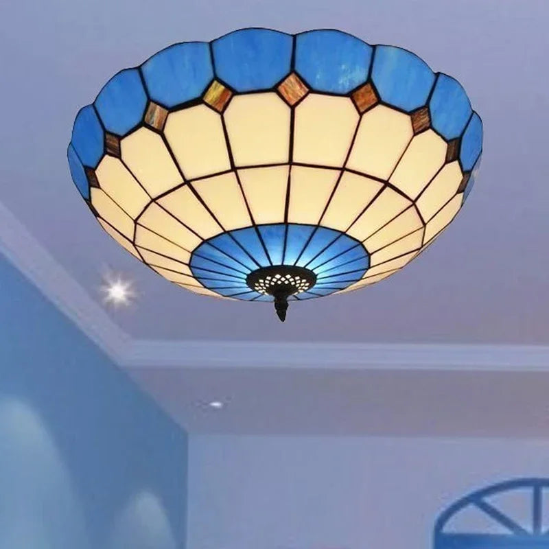 A blue stained glass ceiling light with a scalloped edge installed on a ceiling, with light emanating from it.