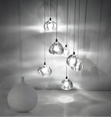 A cluster of clear crystal ball pendant lights hanging in a cascade, with a white vase in the foreground.