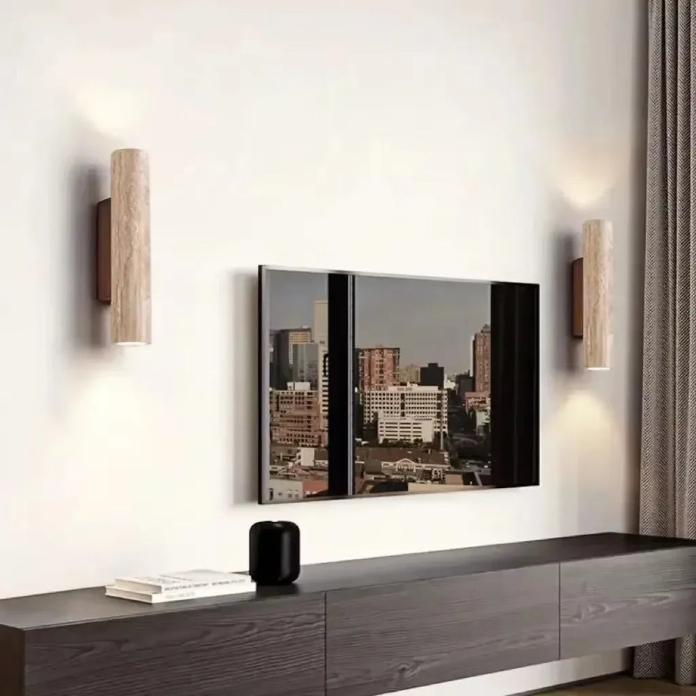 Two cylindrical stone wall sconces flanking a large television on a modern media console in a living room setting.