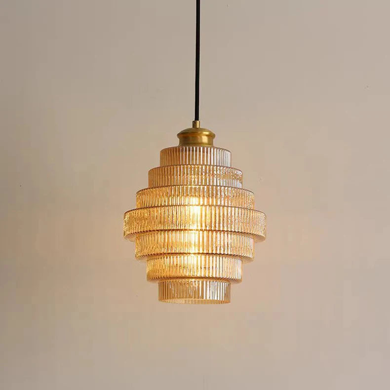A glass tiered pendant light with ribbed glass shades and brass accents, illuminated and hanging in a softly lit room.