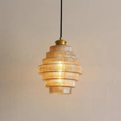 A glass tiered pendant light with ribbed glass shades and brass accents, illuminated and hanging in a softly lit room.