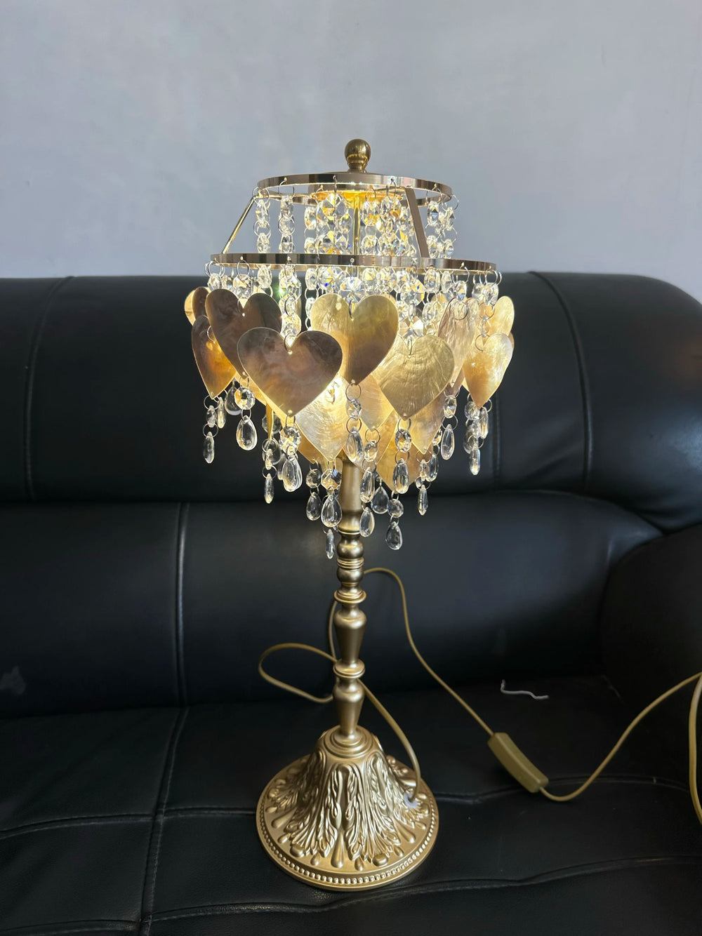 Decorative table lamp with crystal accents and heart designs on a black leather couch.