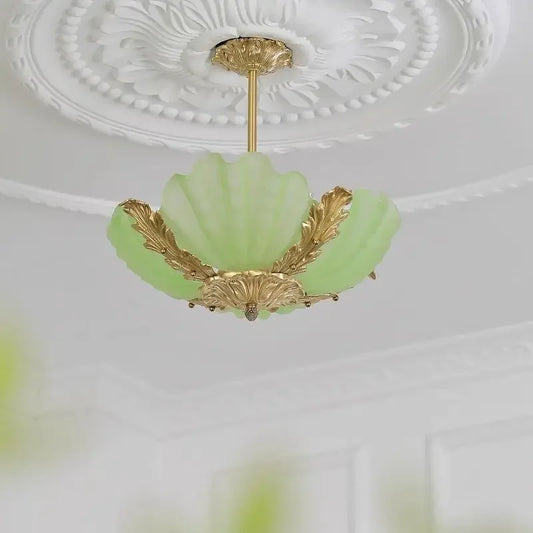 A light green shell-shaped glass pendant light with intricate gold leaf details against a white ceiling.