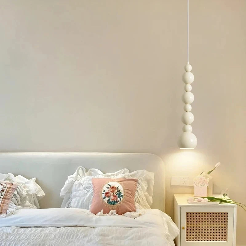 Cream gourd-shaped pendant light hanging over a bed with ruffled pillows.