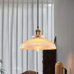 A single fluted glass dome pendant light with a polished copper finish hanging in a well-lit room with sheer curtains in the background.
