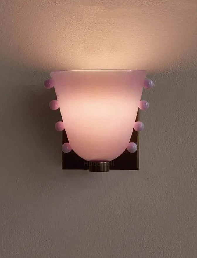 Wall-mounted light fixture with pink glass shade on a gray background