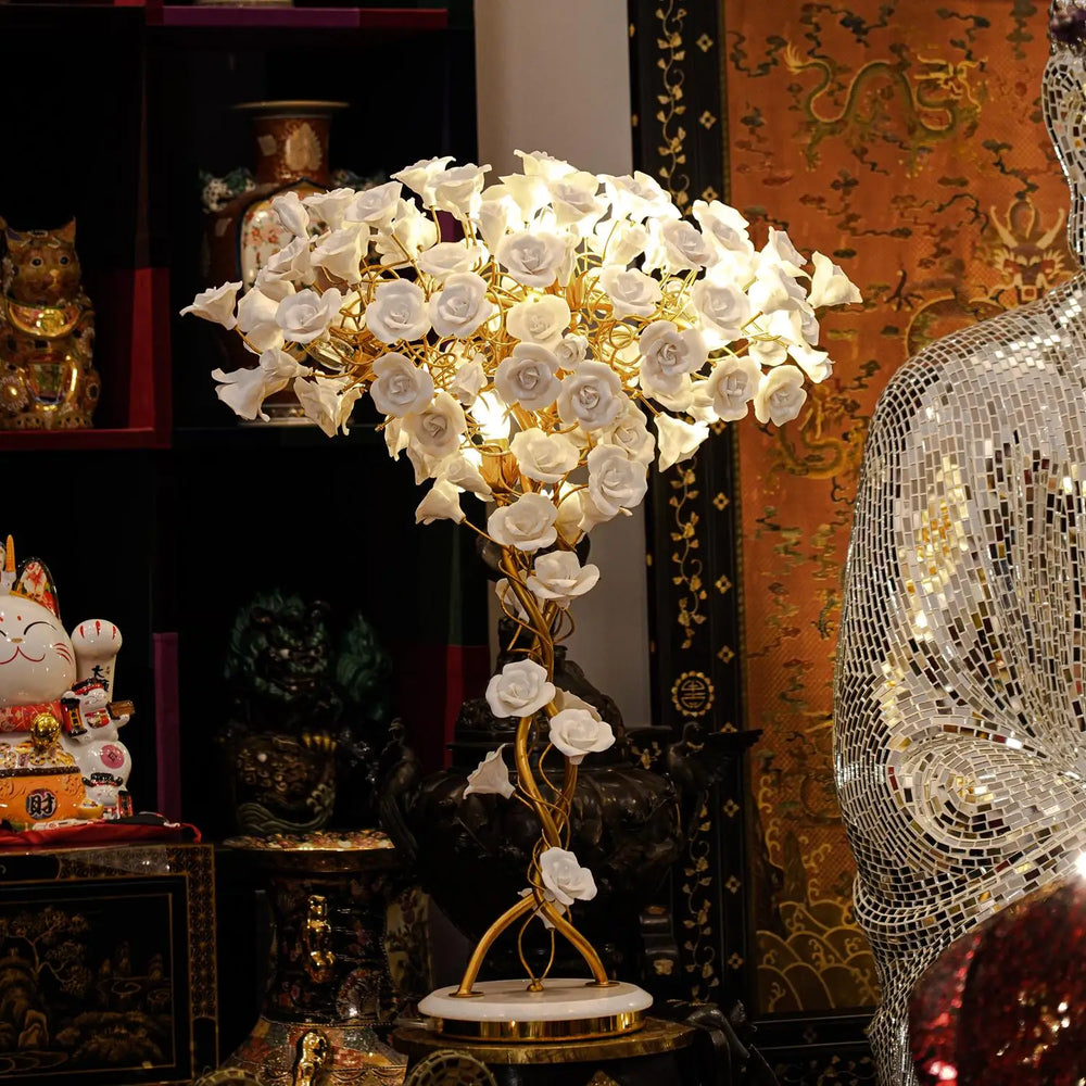 Decorative lamp with white flowers and gold accents in a room with various items.