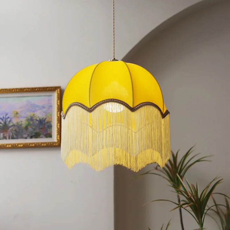 Yellow velvet dome pendant light with long cream fringe hanging from a ceiling.